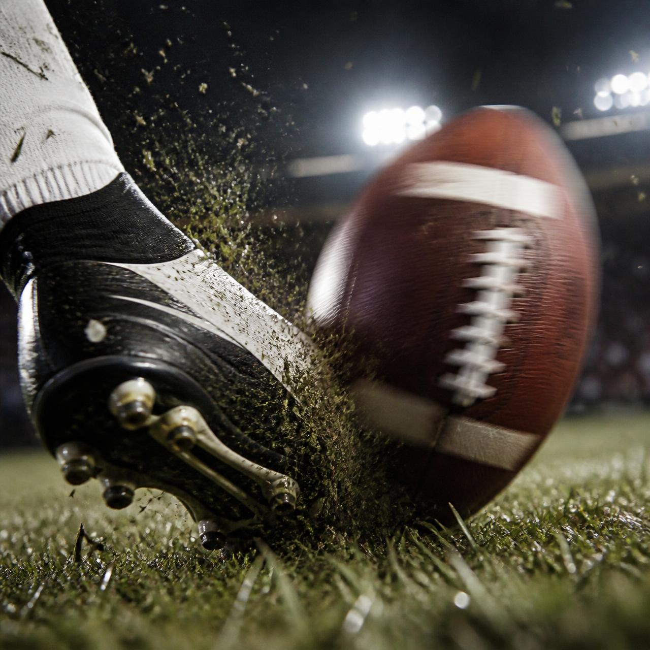 A football player kicking the ball beneath the stadium lights